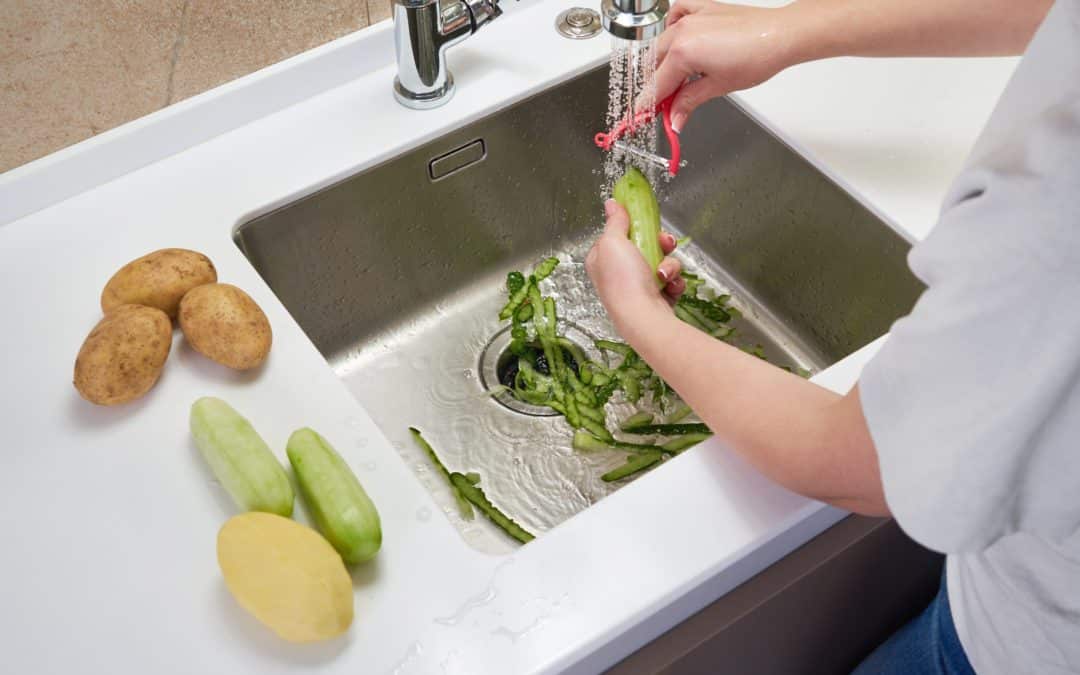 Someone peeling vegetables into kitchen sink