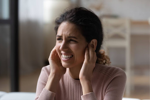 A woman covering her ears because of a loud noise in her home.